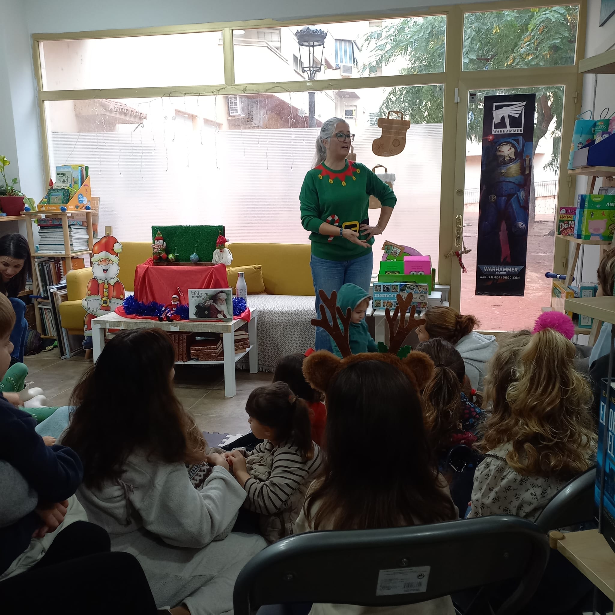 Cuentacuentos de Navidad en Librería La Pluma con niños sentados escuchando a una narradora con jersey navideño.