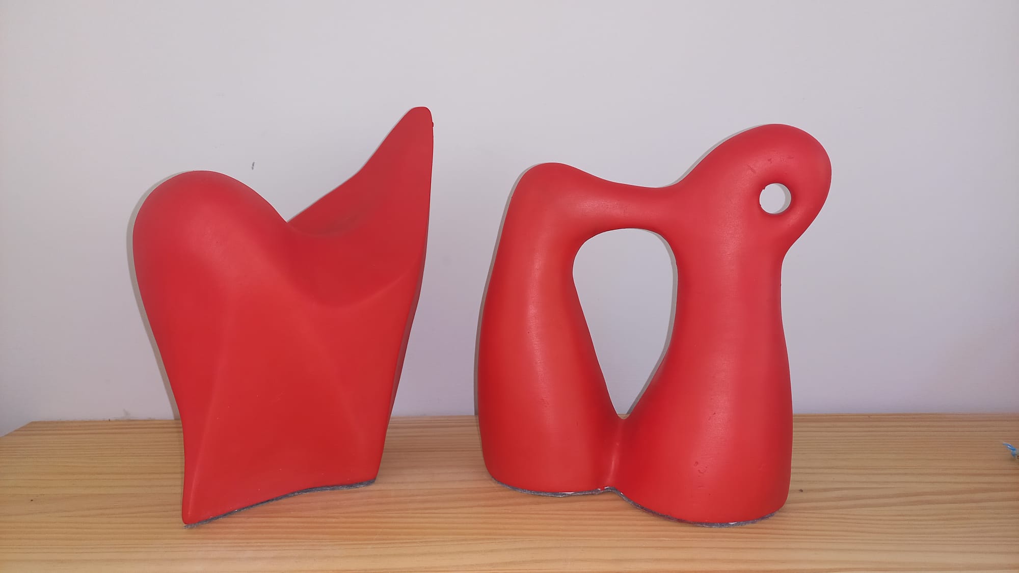 Dos esculturas abstractas de cerámica en color rojo vibrante sobre un estante de madera clara.