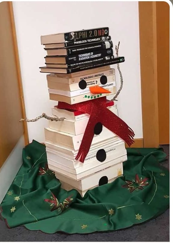 Muñeco de nieve creativo hecho con una pila de libros blancos, una bufanda roja brillante y un gorro de libros negros.